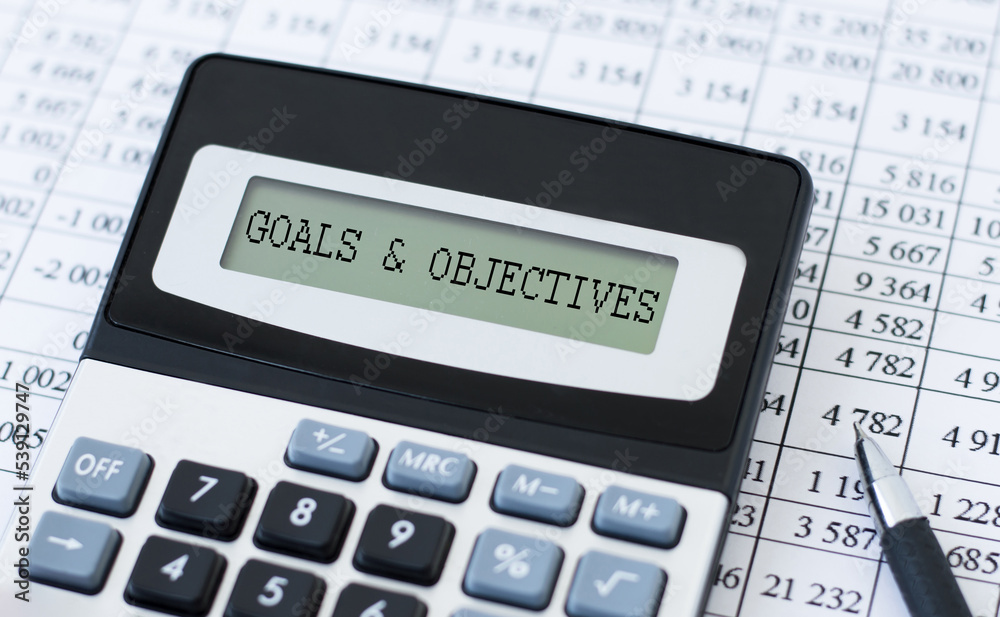 Text Goals and OBJECTIVES on a calculator screen on a table with documents, a business concept Text Goals and OBJECTIVES on a calculator screen on a table with documents, a business concept