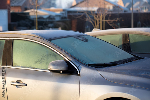 A portrait of the side of a car with frozen side windows and a frozen windshield during winter. The ice first needs to melt or be removed before the driver can safely start the journey.