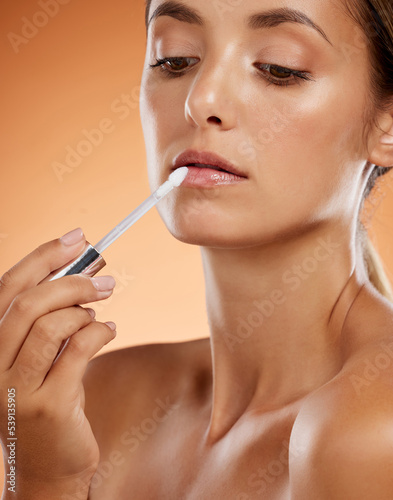 Beauty  makeup and lip gloss with woman in a studio for grooming  hygiene and lips cosmetics. Face  skincare and model apply lipstick against a brown background for full  feminine and natural lip