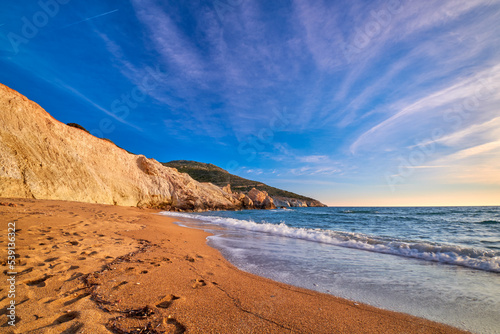 Low sun over beach, cliffs and hills and deep azure sea. Agios Ioannis