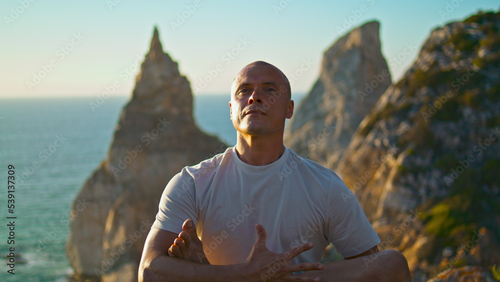 Strong guy exercising yoga at beautiful ocean cliff closeup. Focused fit man