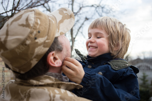 military man standing with his back holds a happy child in his arms. The long-awaited joyful meeting of father and son after military service photo