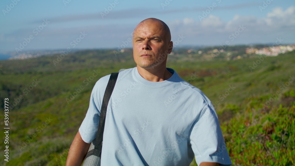 Yoga man going outdoors in sunlight. Focused guy walking green field at ocean