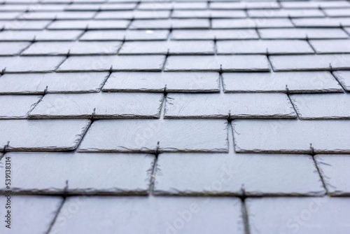A close up portrait of a black, blue slate tile roof. The long lasting natural shingles are placed in a layered pattern and you can see the hooks keeping them in place.