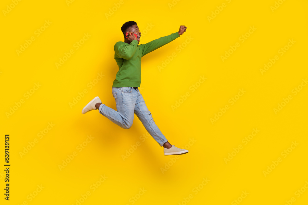 Full length body size view of handsome trendy cheery guy jumping talking on phone isolated on vivid yellow color background