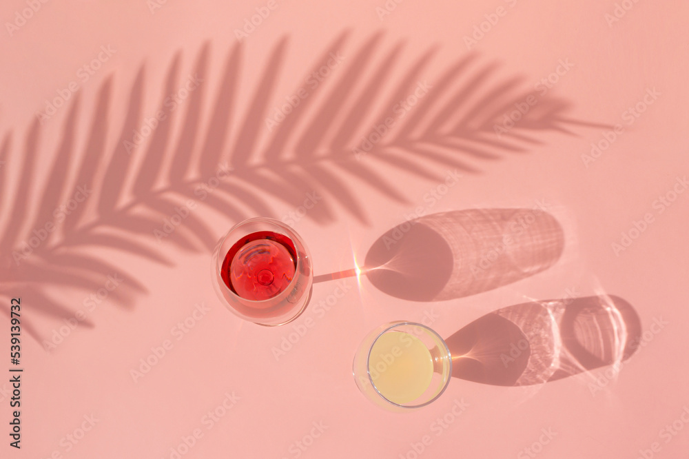 Creative idea with a glass of red wine and lemonade on pink background. The shadow of a palm leaf and glasses on a sunny day. Flat lay.
