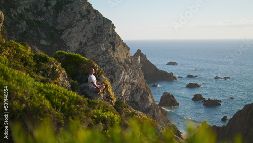 Serene person meditating ocean view. Calm man resting practicing yoga at cliff