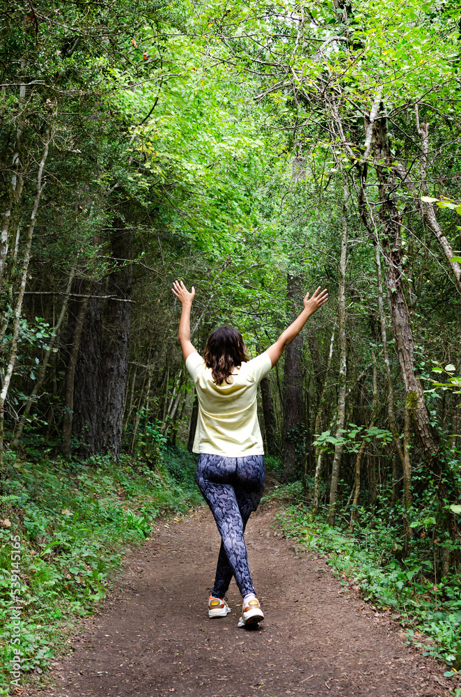 rear view of a young woman raising her arms in the forest. she feels free, strong, grateful and full of vitality. concept of freedom and life.