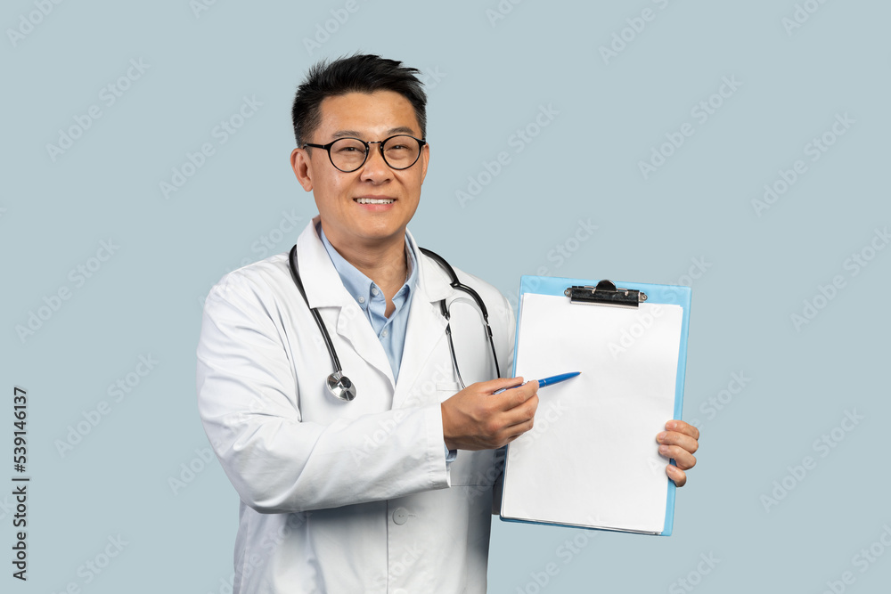 Smiling middle aged chinese male doctor in white coat and glasses shows on tablet with empty space Smiling middle aged chinese male doctor in white coat and glasses shows on tablet with empty space