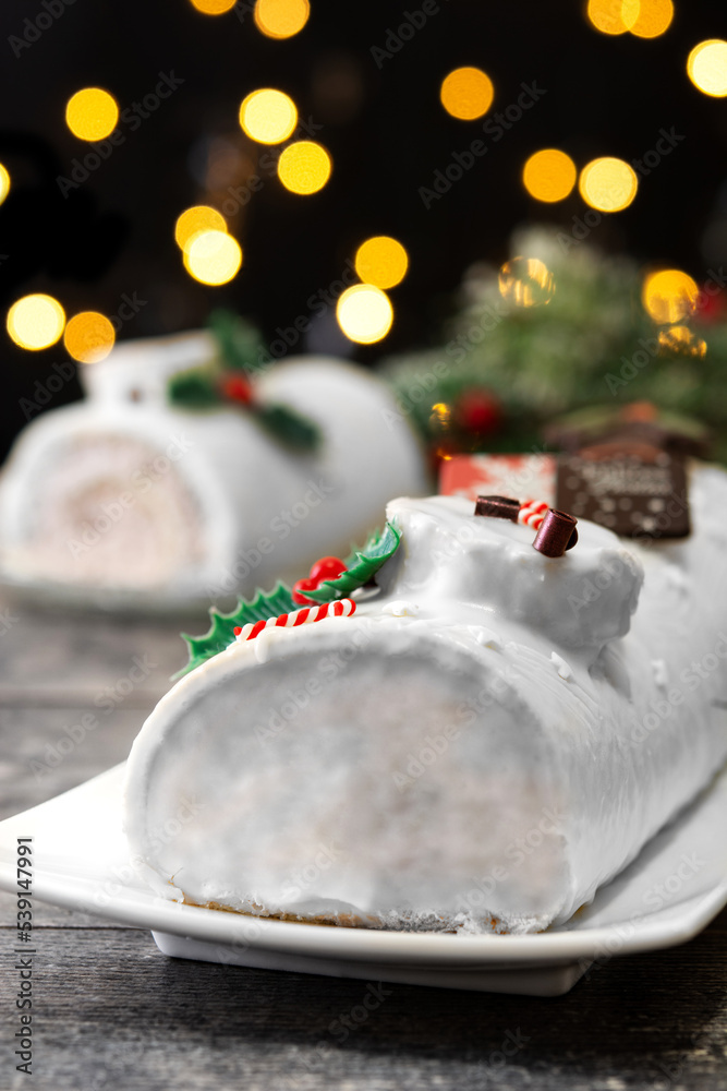 Fototapeta premium White chocolate yule log cake with christmas lights on wooden table