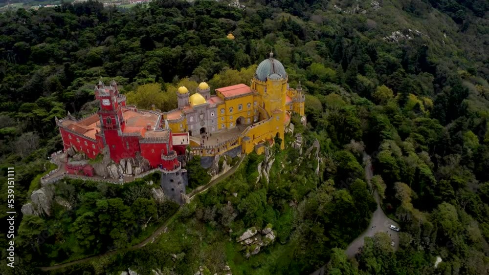 Cinematic aerial perspective of Pena Palace, Sintra, Portugal. Situated in top of a hill in the Sintra Mountains, surrounded by forest. In background Cintra city. Drone backward Cinematic aerial perspective of Pena Palace, Sintra, Portugal. Situated in top of a hill in the Sintra Mountains, surrounded by forest. In background Cintra city. Drone backward