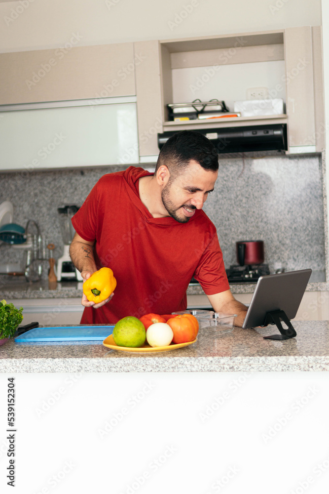 Young man consulting an online recipe with a tablet while preparing a meal in his home kitchen.