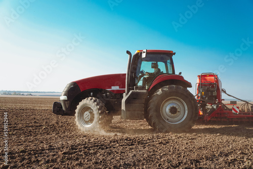 The tractor performs field work. Modern red tractor in the agricultural field. Tractor plowing land.