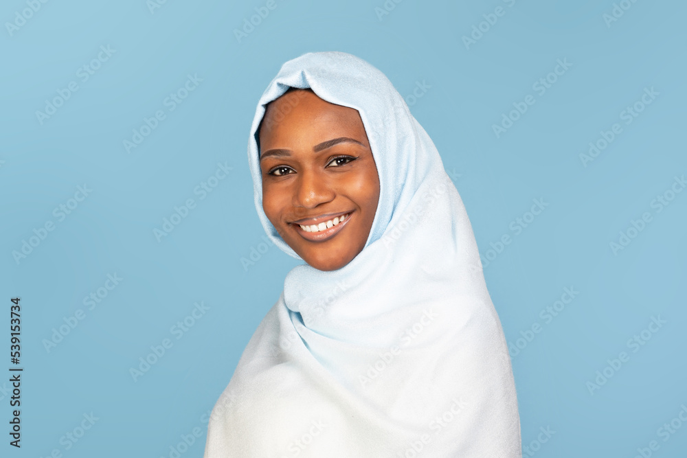 Portrait of happy african american muslim woman in hijab looking and smiling at camera, standing over blue background Portrait of happy african american muslim woman in hijab looking and smiling at camera, standing over blue background