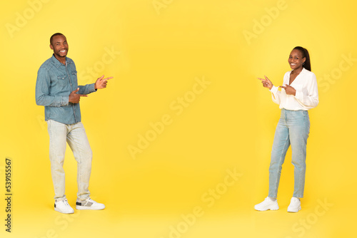 Cheerful African Spouses Pointing Fingers At Free Space, Yellow Background