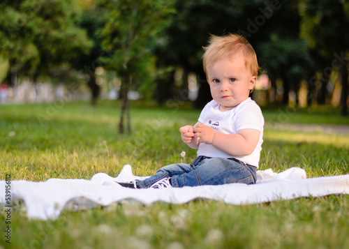 Kid boy blond 2 years old in summer park on the grass