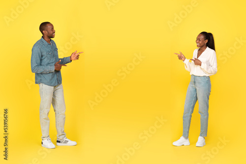Happy Black Couple Pointing Fingers At Each Other, Yellow Background