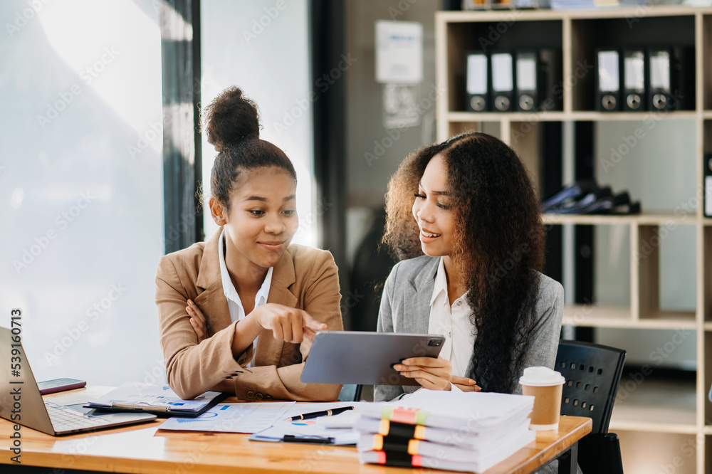 Business colleague business presents and explains and using laptop and tablet. Teamwork, financial marketing team, while sitting in modern office Business colleague business presents and explains and using laptop and tablet. Teamwork, financial marketing team, while sitting in modern office