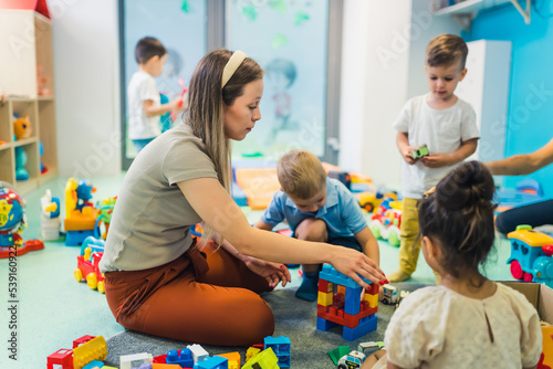 young and beautiful teacher and toddlers playing with building blocks toy at the nursery, full shot. High quality photo