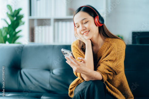 Beautiful young asian woman with headphones relaxing on the sofa. She is listening to music using smartphone . Chill out and leisure concept