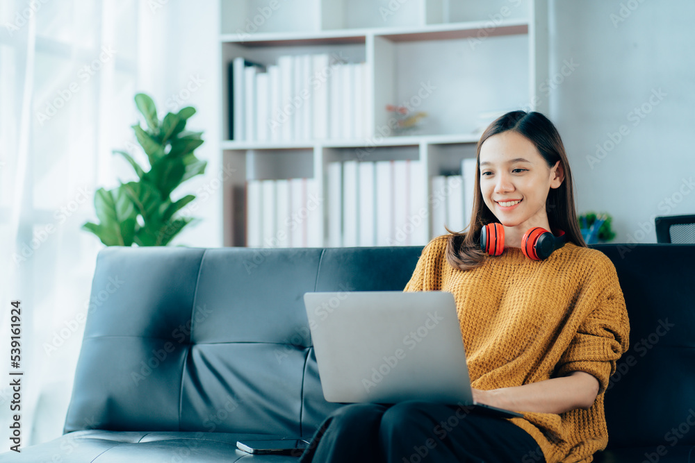 Naklejka premium Beautiful young asian woman with headphones relaxing on the sofa. She is listening to music using smartphone . Chill out and leisure concept