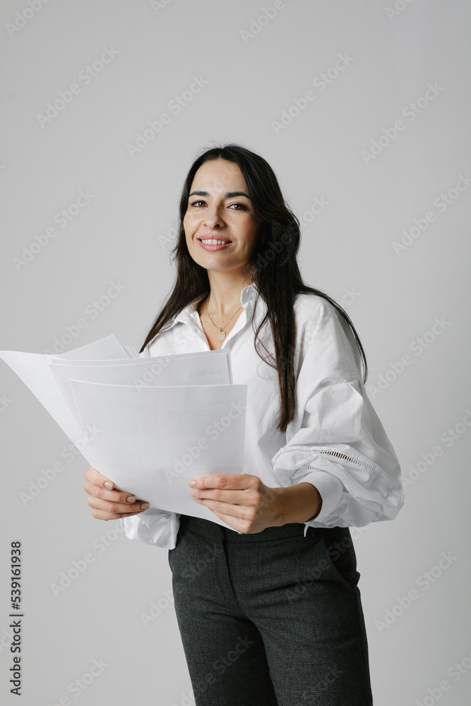 Portrait of middle-aged woman, mentor coach stays over white wall holds papers. Portrait of middle-aged woman, mentor coach stays over white wall holds papers.