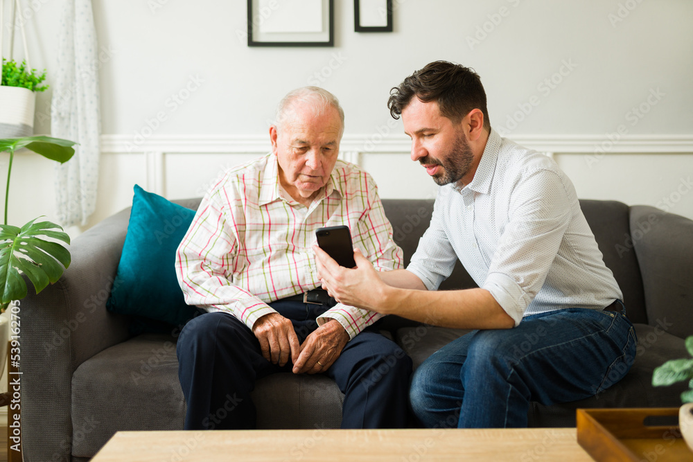 Son helping his elderly father to use smartphone technology