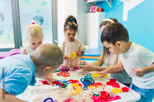 preschoolers enjoying making figures with kinetic sand with their teacher, the development of the fine motor concept. High quality photo