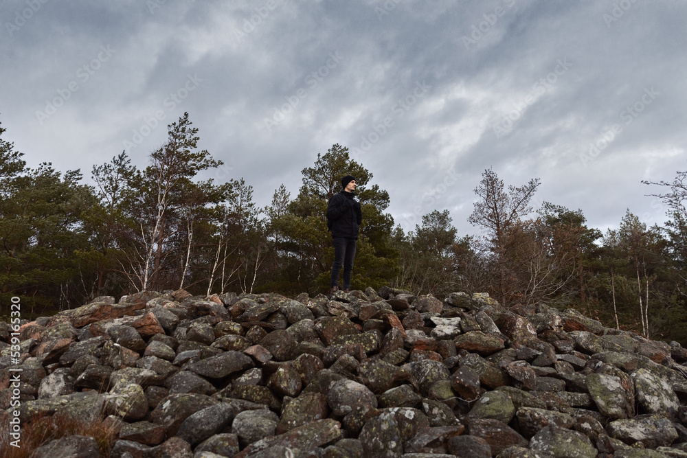 A man with a backpack standing on top of a pile of rocks in the forest