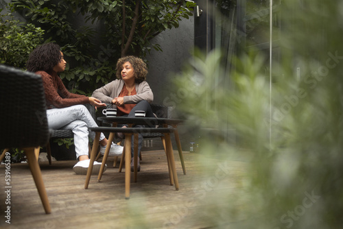 Shot of a young African-American woman bonding with her mother. They sit on the patio and have a coffee.