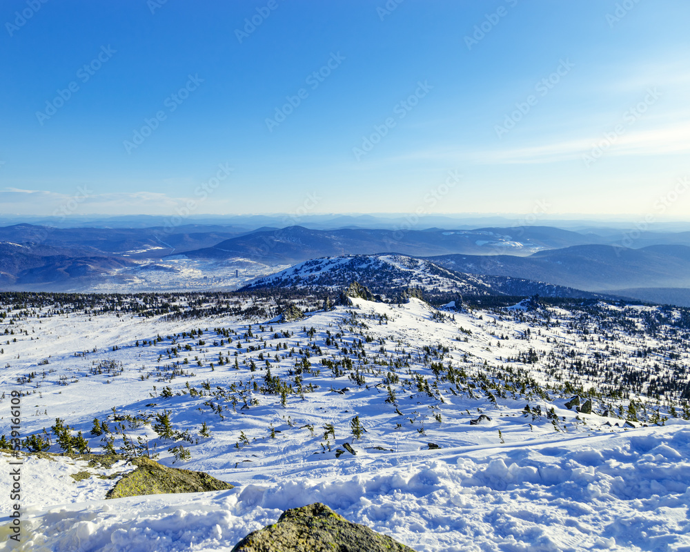 View from mount peak to mountain hills, white snow, blue sky, stones and fir trees. Winter landscape in Gornaya Shoria, Sheregesh ski resort in Russia, Altai mountains nature background.