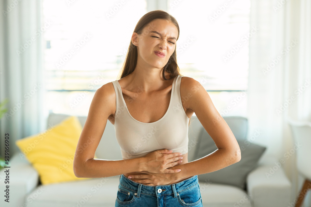 Unhappy Female Suffering From Stomachache Touching Aching Belly At Home