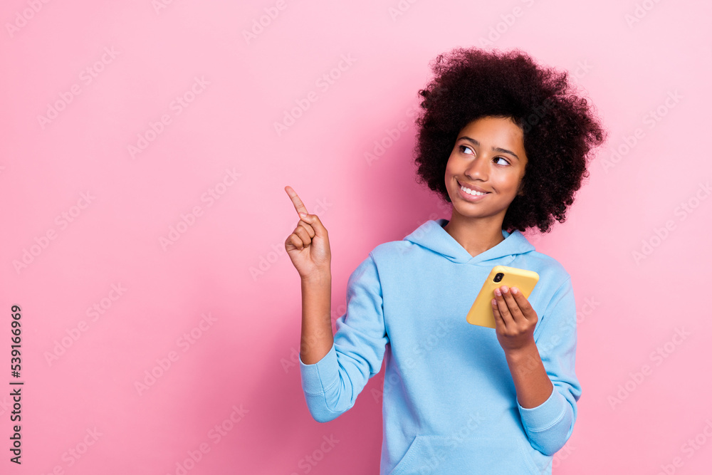 Photo portrait of charming small girl holding smart phone point look empty space wear trendy blue outfit isolated on pink color background Photo portrait of charming small girl holding smart phone point look empty space wear trendy blue outfit isolated on pink color background