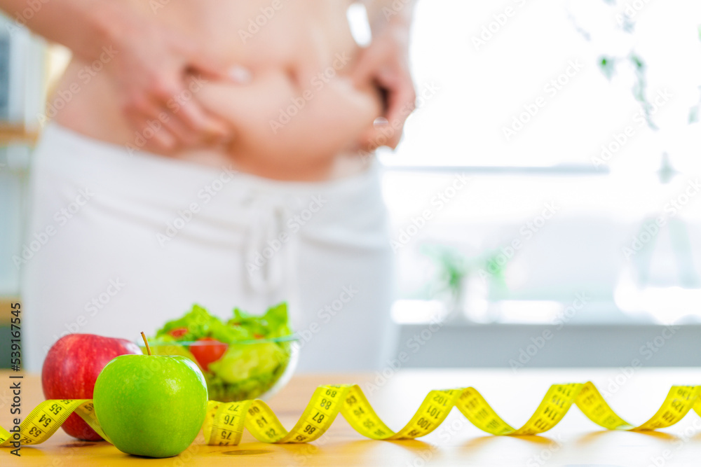 Red and green apple with measuring tape on table with fatty female body at background for diet concept Red and green apple with measuring tape on table with fatty female body at background for diet concept