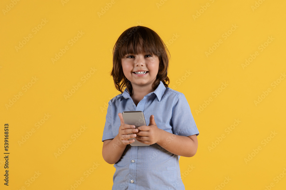 Kids and gadgets. Adorable little boy holding smartphone and smiling to camera, watching videos online, free space Kids and gadgets. Adorable little boy holding smartphone and smiling to camera, watching videos online, free space