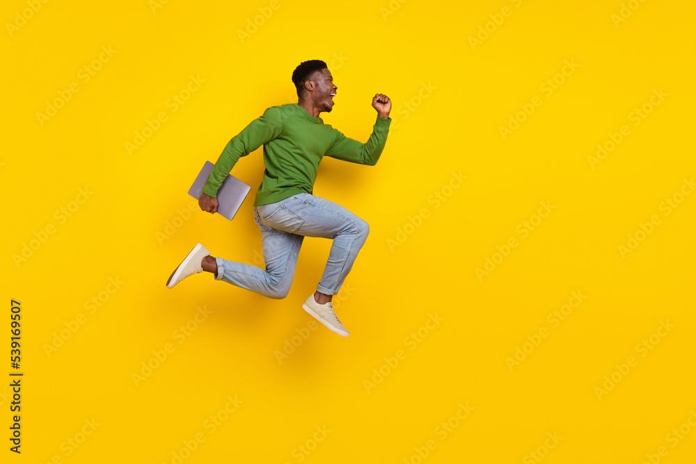 Full length body size view of handsome trendy guy jumping carrying laptop rejoicing isolated over vivid yellow color background