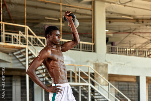 Athletic black young man lifting a heavy-weight in outdoor gym under the bridge. Healthy lifestyle concept