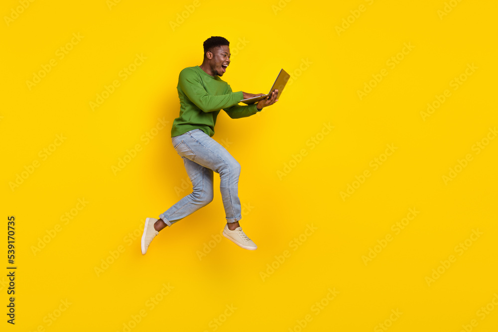 Full length body size view of attractive cheery guy jumping using laptop web order buy isolated over vivid yellow color background