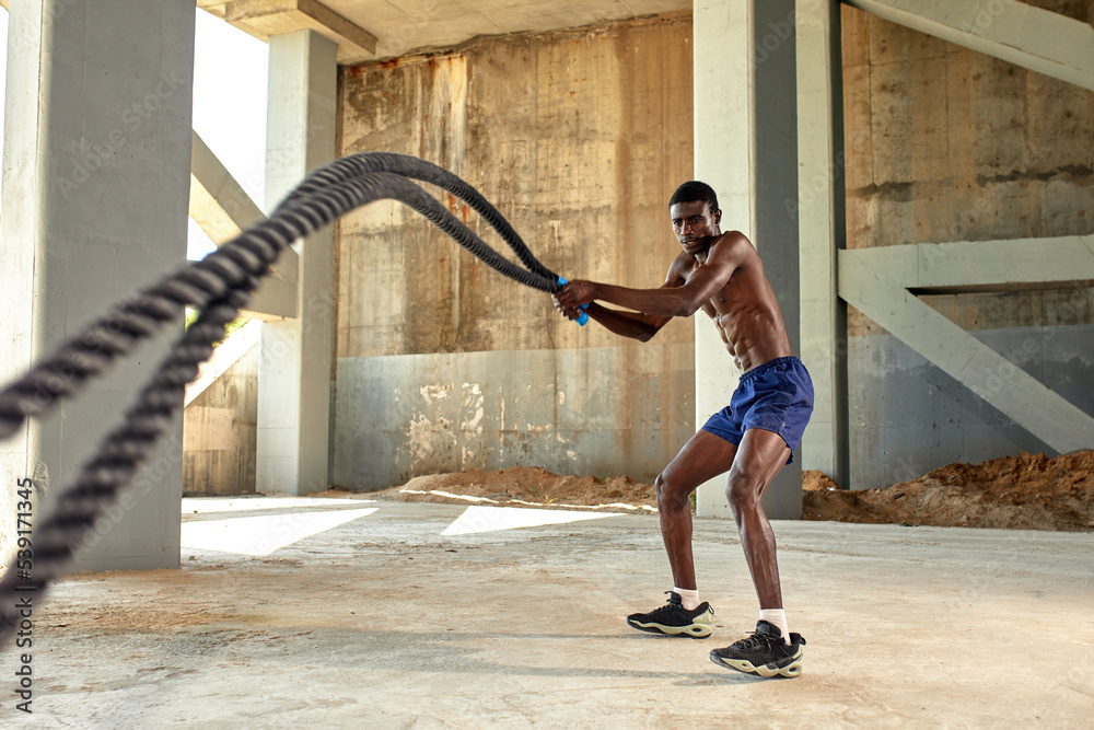 Rope workout. Sport man doing battle ropes exercise outdoor. Black male  athlete exercising, doing functional fitness training with heavy rope Stock  Photo