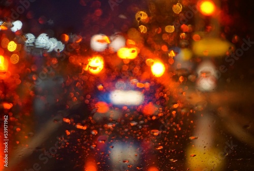 Glasscheibe mit Regentropfenmuster vor Stra  e mit Autoverkehr und roten und goldgelben Lichtern im Dunkeln in der Nacht im Herbst 