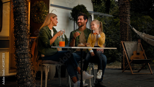 Caucasian family sitting in forest camping vacation outdoor near van eating lunch have picnic with croissants and orange juice mother father and child girl drinking fresh talking refreshing with drink