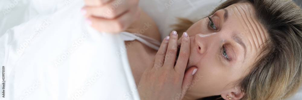 A woman alone in bed looks in surprise under the covers