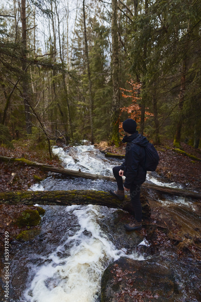 A caucasian man with a backpack standing next to a stream in a forest.