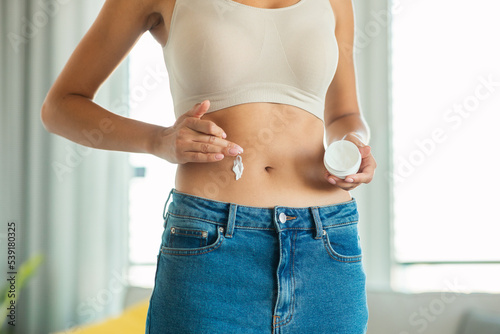 Lady Applying Moisturizer Cream On Belly Standing At Home, Cropped