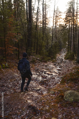 A caucasian man with a backpack walking in a forest on a stone path at sunset.