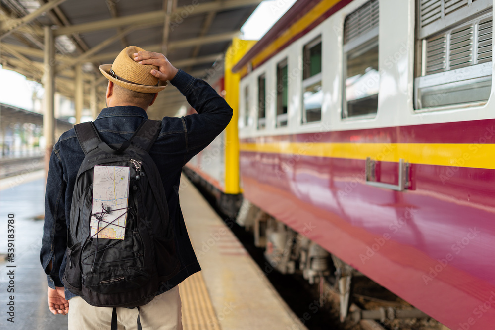 Young asian man traveler backpack in the train station. Backpacker male wear hat and denim jacket at the railway. Travel concept. The concept of a man traveling alone. Young asian man traveler backpack in the train station. Backpacker male wear hat and denim jacket at the railway. Travel concept. The concept of a man traveling alone.