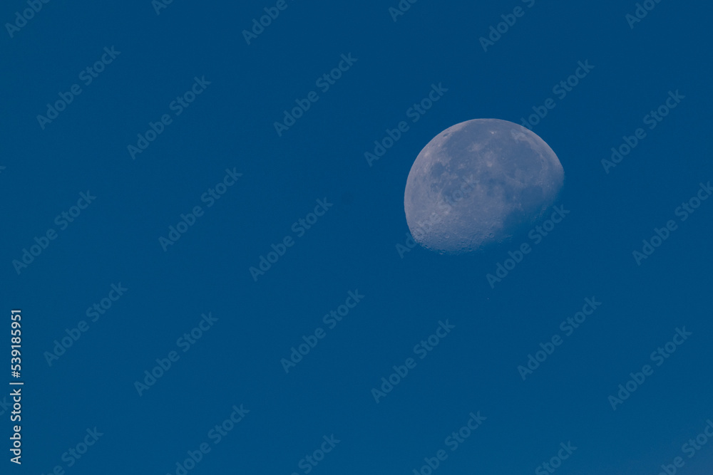Partially illuminated moon during the day against a clear blue sky with copy space