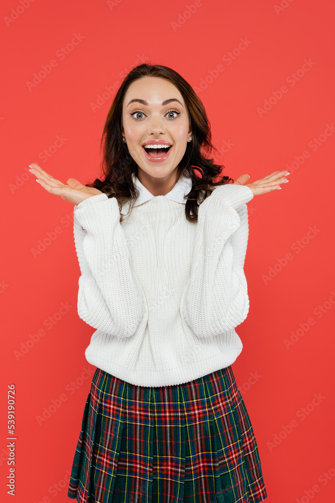 Excited woman in jumper and plaid skirt looking at camera isolated on red Excited woman in jumper and plaid skirt looking at camera isolated on red