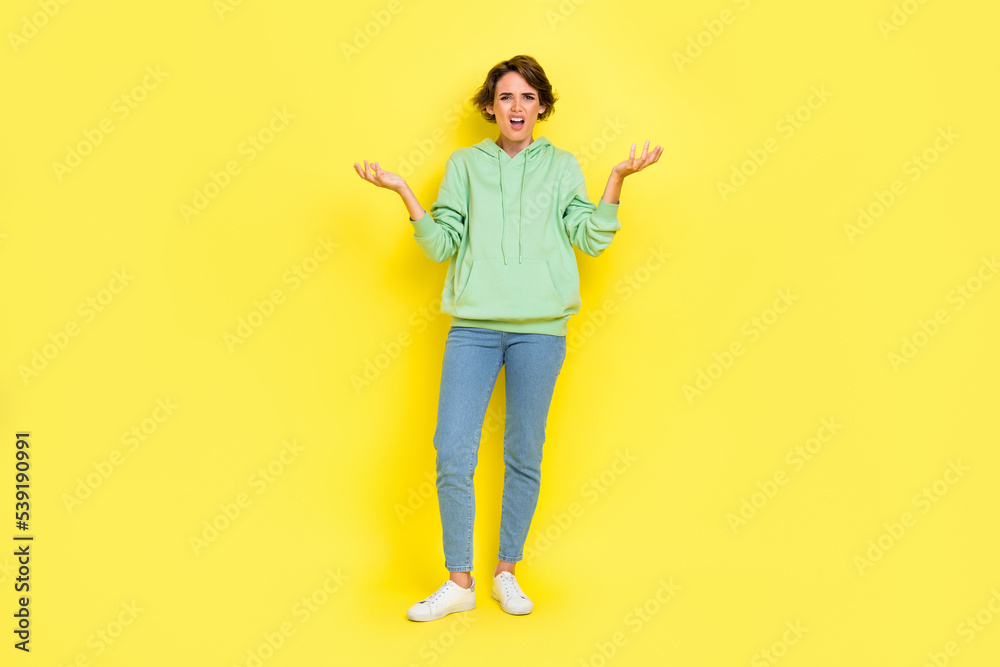 Full length photo of angry surprised lady wear green hoodie screaming rising arms isolated yellow color background Full length photo of angry surprised lady wear green hoodie screaming rising arms isolated yellow color background