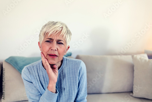 Photo of depressed ill mature woman having toothache and touching cheek. Mature woman suffering from tooth pain, caries. Gray hair female suffering from toothache, closeup.
